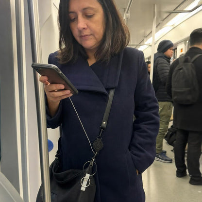 Mujer usando su celular en el Metro con la correa Aferra colgada de la cartera